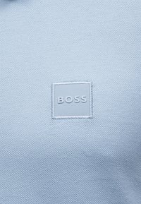 Ανοιχτό μπλε υφασμάτινο με υφή, με ραμμένη τετράγωνη ετικέτα στο κέντρο, με ανάγλυφη την λέξη "BOSS" σε ταιριαστό χρώμα.