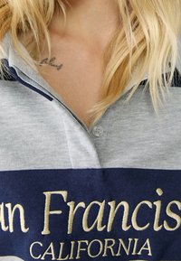 Grijs en marineblauw gestreepte polo shirt met een knoopsluiting bij de kraag, met een geborduurd "San Francisco California" in goud. Soepele katoenen textuur.