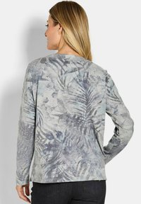 Lange mouwen top in lichtgrijs met een blauw tropisch bladerenpatroon. Gladde textuur, ontspannen pasvorm en ronde hals.