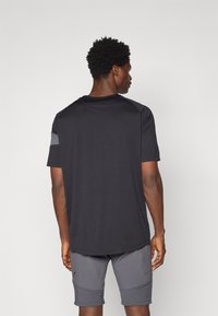 Czarny sportowy t-shirt z krótkimi rękawami, okrągłym dekoltem i szarymi detalami na ramionach; połączony z szarymi szortami z akcentami w formie paneli.