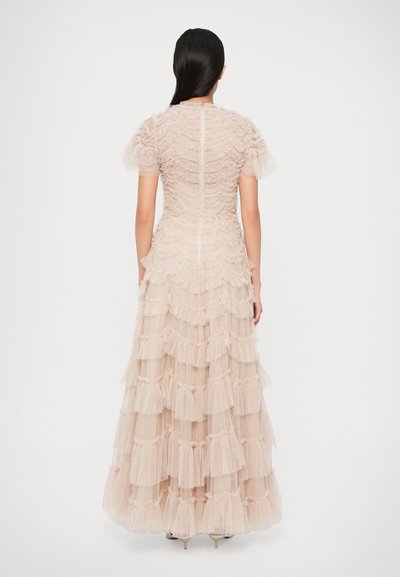 Μακριά τουαλέτα από τούλι σε απαλό μπεζ με κοντά φουσκωτά μανίκια, διαθέτει υφασμάτινη εφαρμογή στην περιοχή του στήθους και ριγωτές κουβέρτες σε όλη τη φούστα.