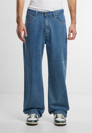 Blå denim jeans med en løs pasform, der har fem lommer, bæltestropper, en frontknaplukning og en subtil logo detalje på låret.