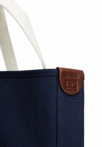 Borsa a tracolla in tela blu navy con manici bianchi e un accento in pelle marrone nella parte superiore, caratterizzata da dettagli cuciti. Design compatto e strutturato.