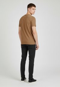 Camiseta de algodón marrón de manga corta, con un diseño ajustado y un escote redondo, combinada con pantalones negros y zapatillas negras. Estilo minimalista.