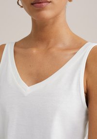 White sleeveless top with a V-neck design, made from a soft fabric with a smooth texture. Subtle stitching detail along the neckline.