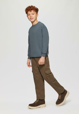 Graublaues Langarm Sweatshirt, olivfarbene Cargo-Hose mit Seitentaschen und braune Wildlederschuhe mit cremefarbigen Sohlen.