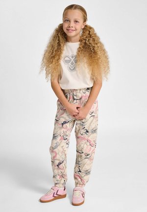 Cremefarbener T-Shirt mit grauem Logo, gemusterte beige Jogginghosen mit rosa-, blau- und grauen Akzenten sowie rosa Turnschuhe mit braunen Sohlen.