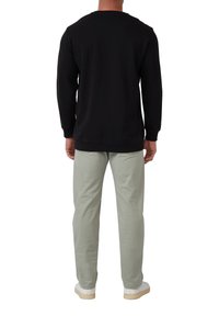 Black sweatshirt with long sleeves, round collar, and ribbed cuffs. Paired with light green trousers and white sneakers. Back view.