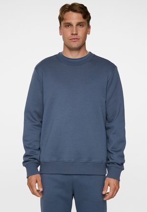 Blue crewneck sweatshirt in soft cotton blend, featuring ribbed cuffs and hem, with subtle branding on the chest. Smooth texture and relaxed fit.