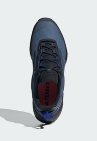 Blå textilskor med svarta detaljer, med en texturerad överdel, snörningsstängning och en vadderad sula synlig genom kragen.