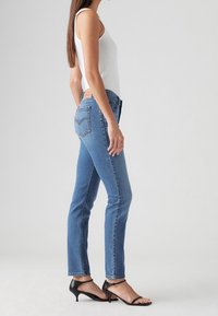 Tunna blå jeans med medelhög midja, tillverkade av denim. Har en bakre logotyppatch och subtila stygn detaljer. Kombinationen med svarta klacksandaler.