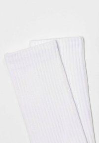 Weiße gerippte Socken mit einer sanften Textur und einem klassischen Design, das sich durch ausgeprägte vertikale Linien und einen umgeschlagenen Bund auszeichnet.