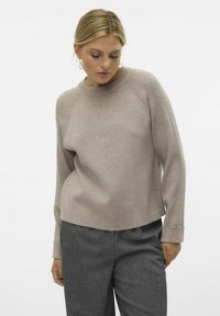 Helle braune Strickjacke mit geripptem Kragen und Ärmelabschlüssen, in lockerer Passform. Kombiniert mit grauen, taillierten Hosen. Glatte Textur, minimalistisches Design.