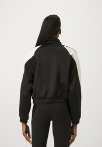 Giubbotto bomber nero con colletto alto, accenti bianchi sulle spalle e orlo elasticizzato. Texture liscia, design aderente.