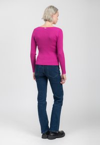 Getailleerde roze geribbelde trui met lange mouwen, ronde halslijn en achteretiket detail, gecombineerd met donkerblauwe uitlopende jeans en zwarte platformschoenen.