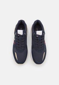 Navy sneakers with a smooth fabric upper, gold accents, and white rubber sole. Features laces and branding on the tongue.