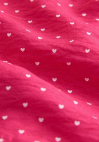 Roze stof met kleine witte hartpatronen, gladde textuur, licht gekreukt, waarbij het speelse ontwerp en kleurcontrast worden benadrukt.