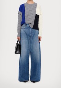 Gebreide trui met meerkleurige panels in grijs, blauw en crème; wijde lichtblauwe jeans; zwarte handtas; casual outfit.