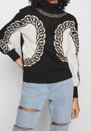 Pull à col roulé noir avec motif chaîne beige sur les manches et le devant, assorti à un jean déchiré bleu clair.
