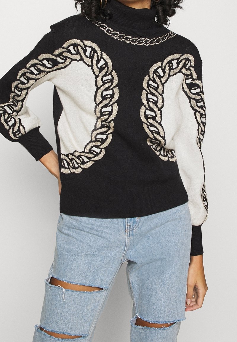 Pull à col roulé noir avec motif chaîne beige sur les manches et le devant, assorti à un jean déchiré bleu clair.