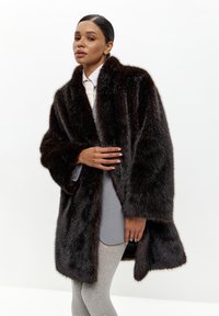 Brun faux fur frakke med en bred krave, oversized pasform og lange ærmer, lagd over en lysegrå top og matchende grå leggings.