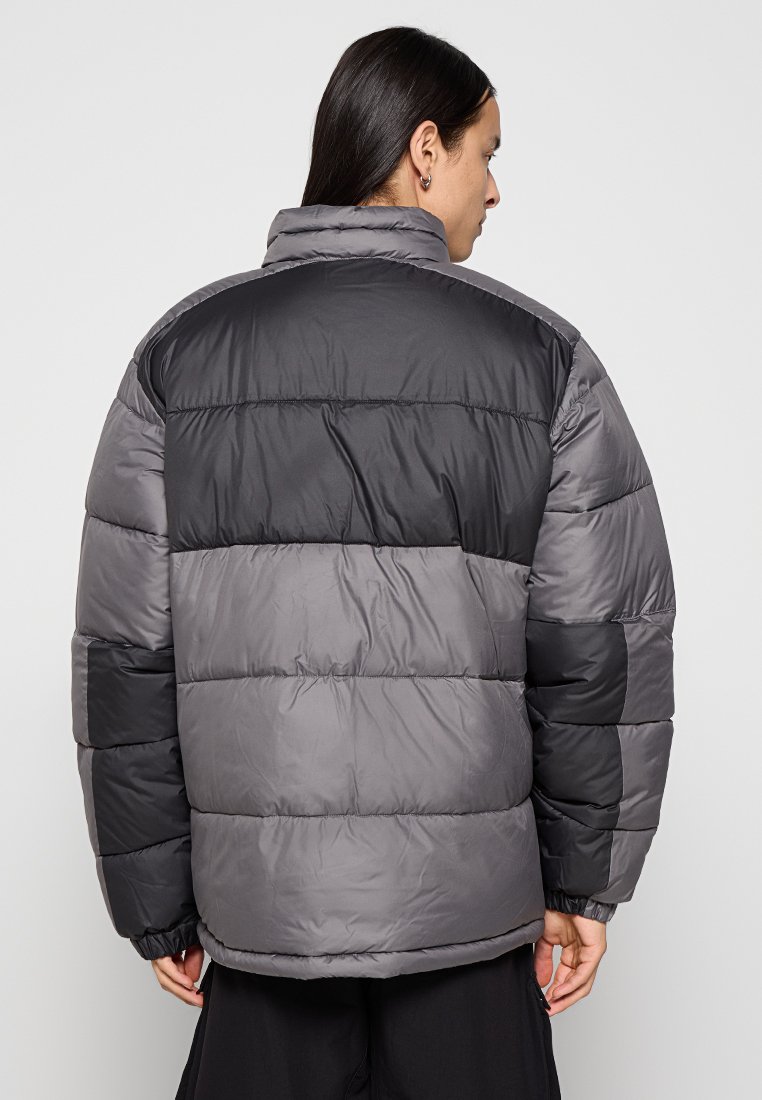 Chaqueta acolchada en tonos grises con una mezcla de secciones oscuras y claras. Presenta un cuello alto y puños elásticos para un mejor ajuste y calidez.