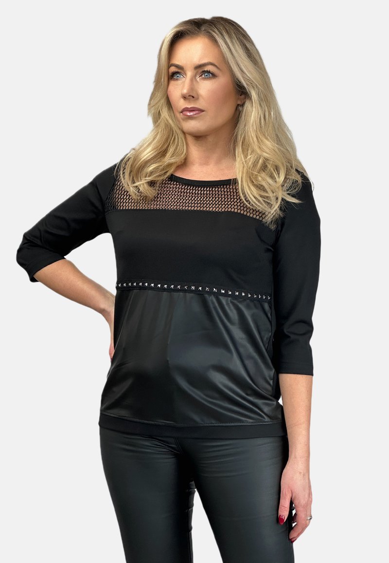 Czarna bluzka z siateczkowym panelem, rękawami o długości trzech ćwiartek oraz błyszczącą dolną częścią w stylu skóry, ozdobioną ćwiekami. Stylizowana z czarnymi spodniami.