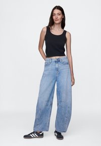 Top corto negro sin mangas combinado con jeans de pierna ancha en azul claro, con costuras distintivas y un ajuste relajado, complementado con zapatillas negras.