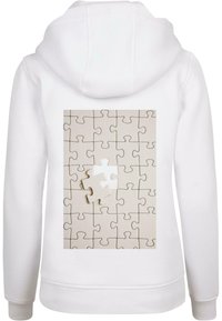 Fehér kapucnis pulóver, amelyen egy világos színű puzzle grafikája látható, egy hiányzó darabbal. A grafikán egymásba illeszkedő formák és sima textúra látható.