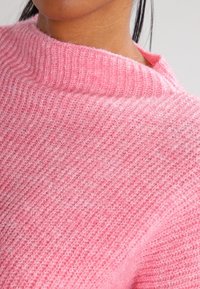 Rosa Strickpullover mit gerippter Struktur und weitem Ausschnitt, der Weichheit und ein leicht flauschiges Finish zeigt.