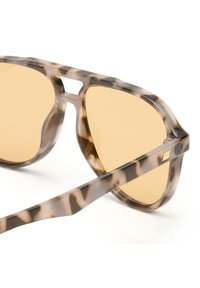 Okulary przeciwsłoneczne w brązowym muszkatołowym kolorze, przezroczystym oprawie oraz jasnobrązowych szkłach. Oprawa ma lekko kanciasty kształt i mały akcent na zausznikach.