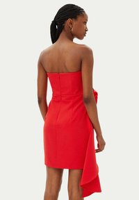 Abito rosso senza spalline con corpetto aderente, chiusura con zip sul retro e un drappeggio fluido all'orlo. Tessuto dalla texture liscia e silhouette elegante.