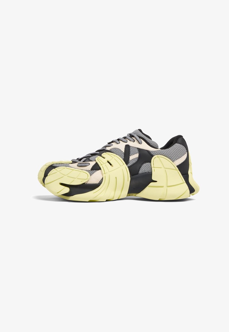 Lace-up sneakers featuring a mesh upper in gray and cream, with black accents and a chunky yellow sole, highlighting unique design elements.