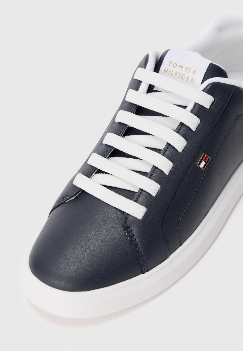 Zapatilla de cuero azul marino con cordones blancos, suela blanca y logo de Tommy Hilfiger en la lengüeta y en el costado.