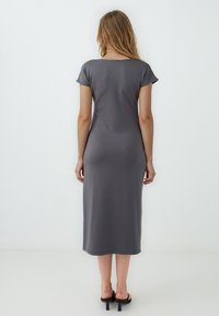 Robe grise, arrivant aux genoux, avec des manches courtes et un col arrondi. Fabriquée en tissu doux, elle présente une silhouette ajustée. Portée avec des sandales noires.
