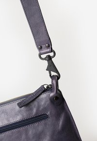 Borsa a tracolla in pelle viola con tasca con zip, una tracolla robusta con dettagli in metallo e una finitura testurizzata.