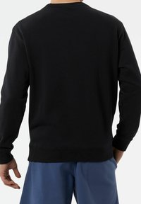Felpa nera con maniche lunghe, collo rotondo, polsini e orlo a costine, realizzata in un tessuto liscio. Indossata con pantaloni corti blu.