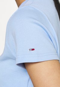 Light blue cotton T-shirt with short sleeves, featuring a ribbed texture and a small embroidered logo in red, white, and blue on the sleeve.
