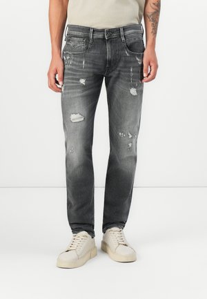 Grå slitna jeans med flera hål, slim fit och en urtvättad finish. Kombinerade med krämfärgade sneakers. Raka framfickor och metallknapp.