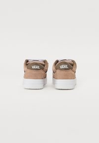 Zapatillas de ante marrón con suelas de goma blanca, que cuentan con cuellos acolchados y un logotipo en el talón. Diseño minimalista con rayas en contraste.