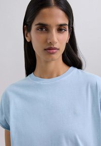 Camiseta de manga corta azul claro hecha de algodón suave, con un sutil logo bordado en el pecho y un clásico cuello redondo.