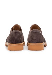 Zapatos de ante marrón con una textura suave, suelas de goma y mediasuelas de color marrón claro que contrastan. Presentan costuras en forma de ondas y un diseño minimalista.