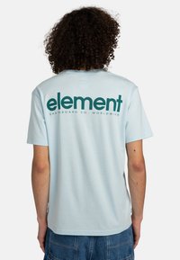 Lyseblå kortærmet t-shirt lavet af bomuld, med stort mørkegrønt "element" tekst og logo på ryggen, glat tekstur.