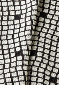 El tejido de punto presenta un patrón de cuadrícula de cuadros negros sobre un fondo crema, mostrando un diseño texturizado y tejido con tamaños de cuadros variados.