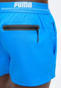 Μπλε αθλητικό σορτς με μαύρη τσέπη με φερμουάρ στο πίσω μέρος και λευκό λογότυπο Puma στη ελαστική μέση.