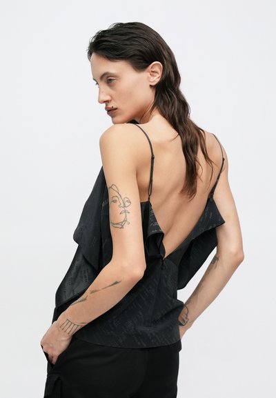 Top nero senza maniche con design drappeggiato, schiena scoperta, spalline sottili e una texture a motivo sottile, abbinato a pantaloni neri.