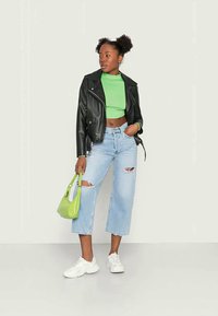 Jaqueta de couro preta, top cropped verde, jeans rasgados de denim azul claro, ténis brancos e uma pequena mala verde. Cabelo em dois coques fofos.