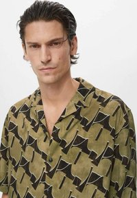 Chemise à manches courtes en tissu léger, avec un motif abstrait vert et noir, col classique et deux boutons sur le devant.
