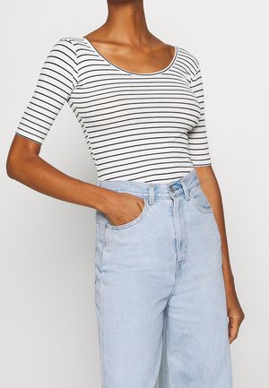 Prążkowany top z krótkim rękawem w biało-czarne pasy, z dekoltem w łódkę. Połączony z jasnoniebieskimi, wysokim stanem jeansami, podkreślający casualowy wygląd.