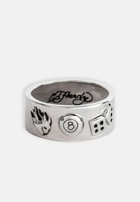 Anillo de metal plateado con diseños en relieve: una huella de pata, una bola 8 y dados. Superficie lisa con un acabado pulido. Firma interna grabada.